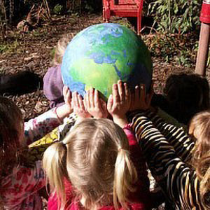 children gathered around a globe with their hands on it.